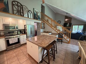A spacious kitchen with granite countertops, stainless steel appliances, and a wooden staircase leading to a living area.
