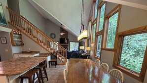 Eine geräumige Küche mit einem großen Esstisch aus Holz, einer Kochinsel und einer Treppe zu einem Erkerraum.