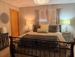 Quarto com cama, abajures, porta de madeira e um objeto decorativo na parede.