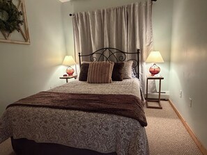 A bedroom with a bed, two bedside lamps, a headboard, and a curtain.