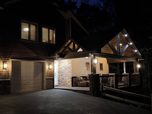 Uma casa de dois andares com garagem, fachada de pedra e varanda coberta com assentos.
