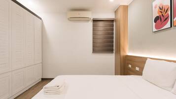 A hotel room with a bed, a wardrobe, an air conditioning unit, and a window with blinds.