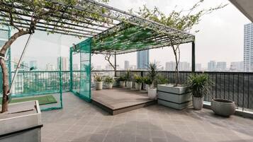 A rooftop terrace with a pergola, potted plants, and a view of the city skyline.