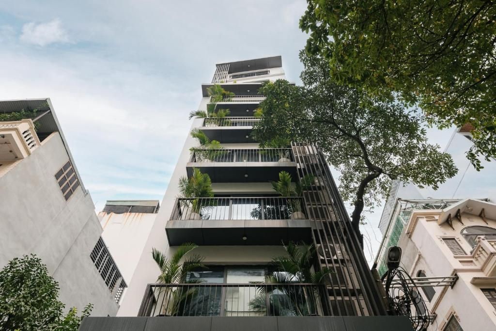 A multi-story building with balconies, a tree in the foreground, and a clear sky.
