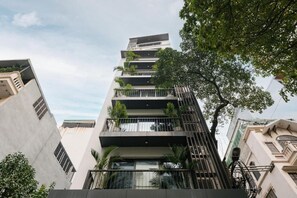 Un edificio de varios pisos con balcones, un árbol en primer plano y un cielo despejado.