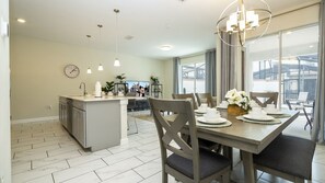 Een moderne keuken met een centraal eiland, een eethoek met stoelen en een tafel voor vier personen, en een groot raam met uitzicht op het omliggende landschap.