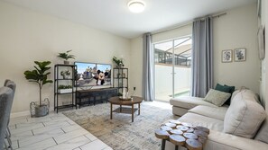 Een woonkamer met een televisie, bank, salontafel en planten.