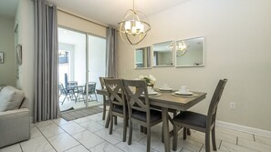 A dining area with a table set for four, chairs, a chandelier, and a sliding glass door leading to a balcony. - 4BR Storey Lake Private Pool & BBQ Near Disney (Kissimmee)