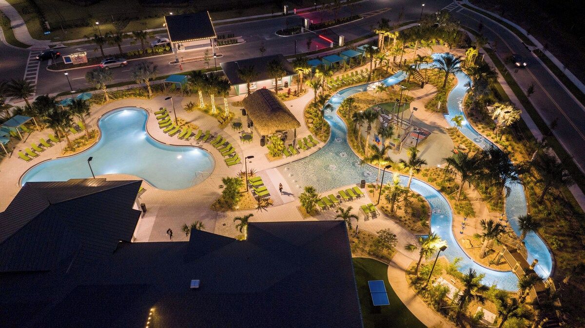 Vue aérienne d’un complexe hôtelier doté d’une grande piscine, d’espaces paysagers aménagés et d’une route à proximité.
