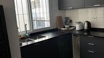 A modern kitchen with dark cabinetry, a stainless steel sink, and a window with a view of buildings outside.