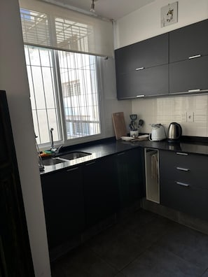 Una cucina moderna con mobili scuri, un lavello in acciaio inossidabile e una finestra che si affaccia su edifici.