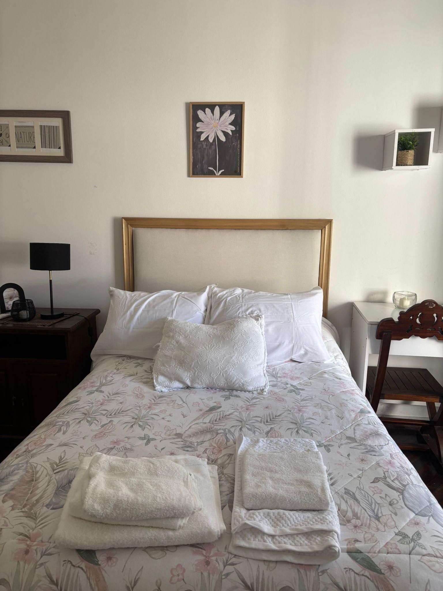 A neatly made bed with floral bedding, a headboard, and two folded towels.