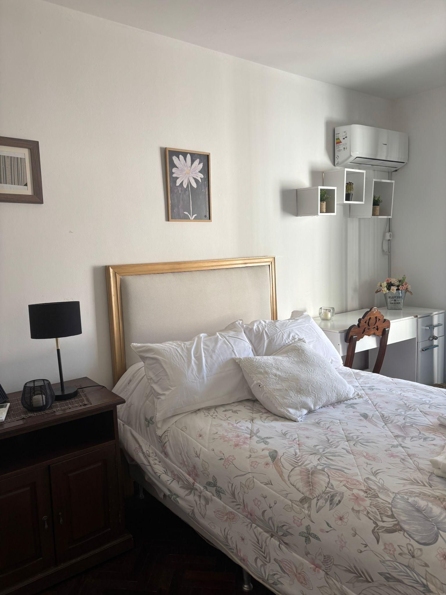 A neatly made bed with a floral bedspread, a bedside lamp, and a framed picture on the wall.