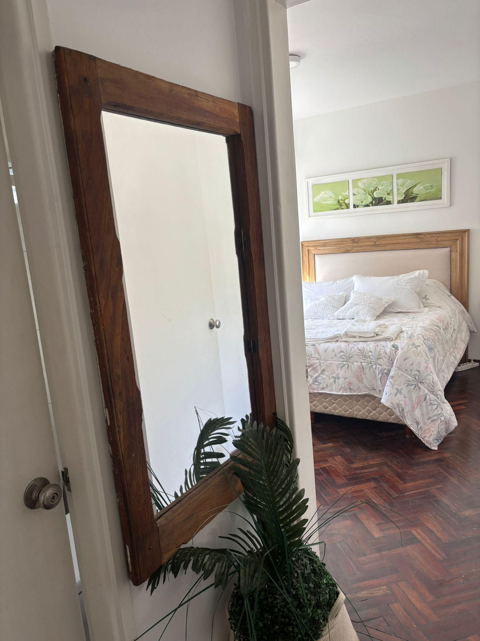 Un dormitorio con una cama, un espejo con marco de madera y una planta en maceta.