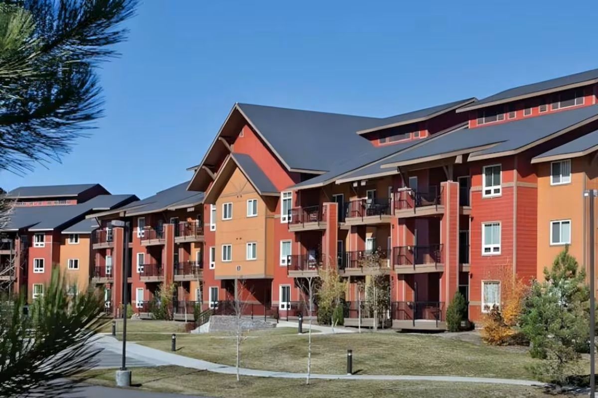 Un immeuble résidentiel à plusieurs étages, doté de balcons, d’un toit plat et surplombant un ciel dégagé.