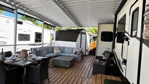 An RV with a covered deck, a sofa, dining table, and chairs. - Well stocked 5th wheel and private space at Christina Lake Resort. (Christina Lake)