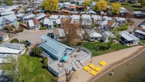 A residential area with multiple houses, a large building with a blue roof, and a sandy beach area with yellow umbrellas. - Well stocked 5th wheel and private space at Christina Lake Resort. (Christina Lake)