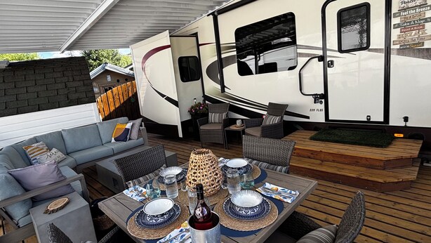 A covered outdoor patio with a dining table set for four, surrounded by wicker chairs and a sofa. - Well stocked 5th wheel and private space at Christina Lake Resort. (Christina Lake)