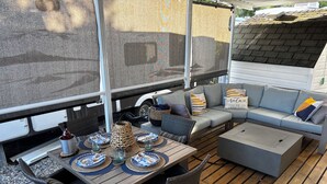 An RV with a covered outdoor area featuring a dining table set with plates and glasses, a woven centerpiece, and a gray sofa with cushions. - Well stocked 5th wheel and private space at Christina Lake Resort. (Christina Lake)