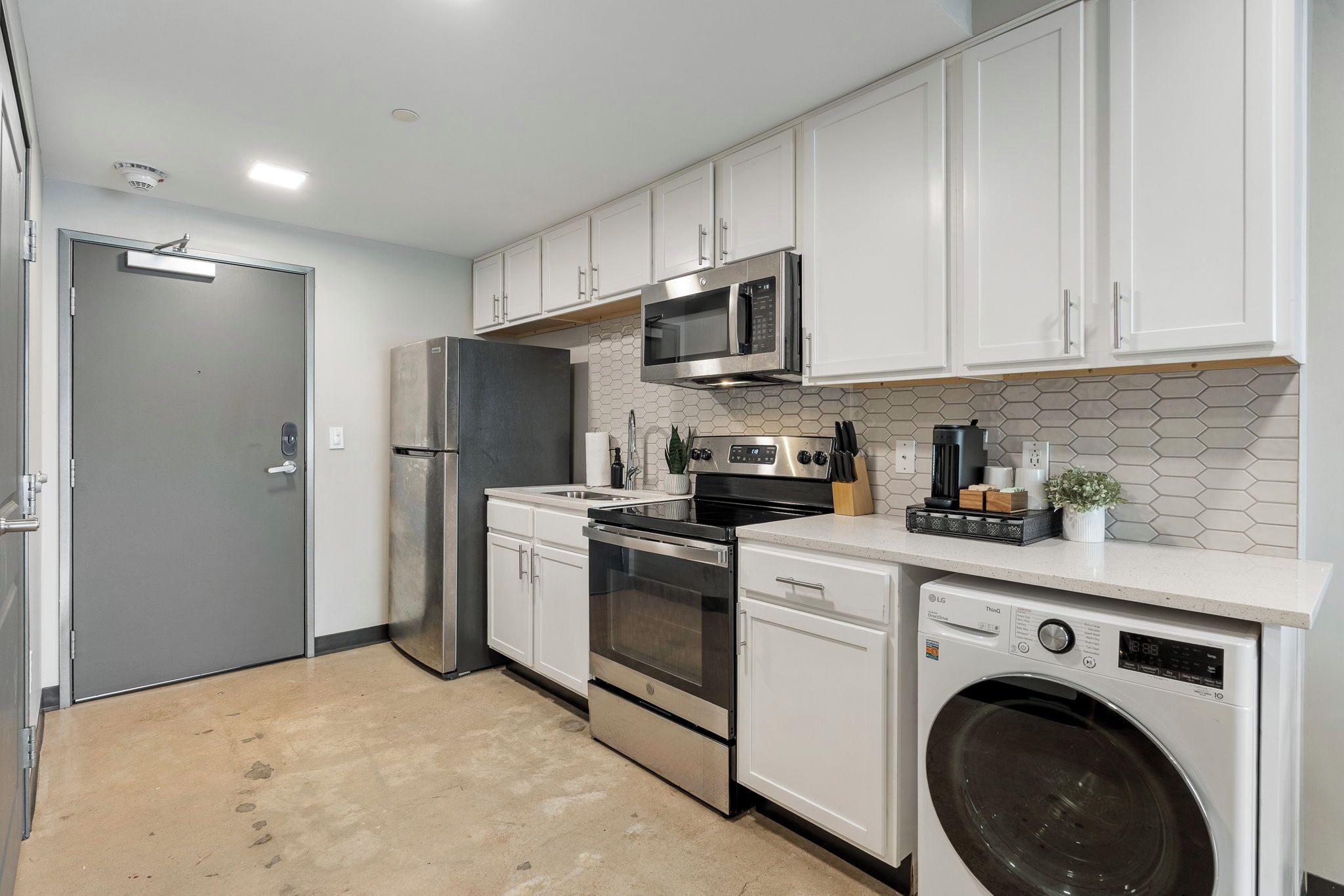 A compact kitchen with white cabinets, stainless steel appliances, a microwave, oven, dishwasher, and a washing machine.