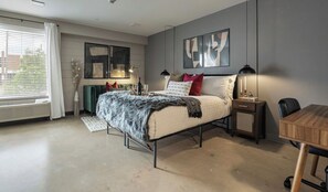 Une chambre à coucher moderne, avec un lit, des tables de chevet, un bureau et des œuvres d’art accrochées aux murs.