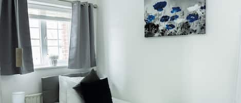 Un dormitorio con una cama, una mesita de noche, una lámpara, una ventana con cortinas y un cuadro en la pared.