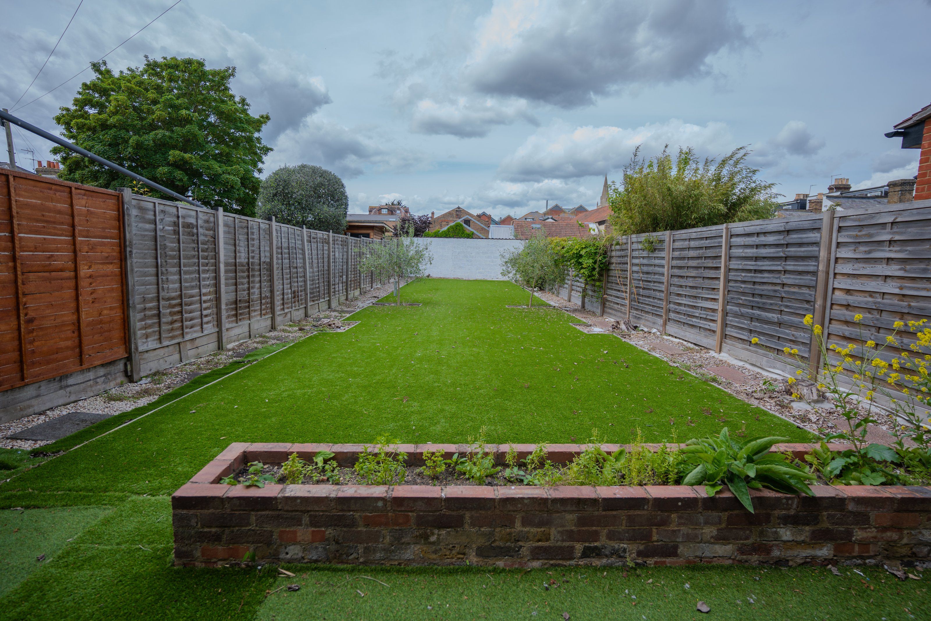 A rectangular lawn with a brick planter box in the foreground, surrounded by a wooden fence.