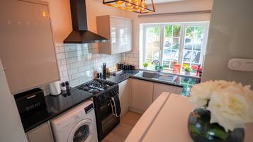 A modern kitchen with a gas stove, oven, washing machine, and a window with a view of parked cars.