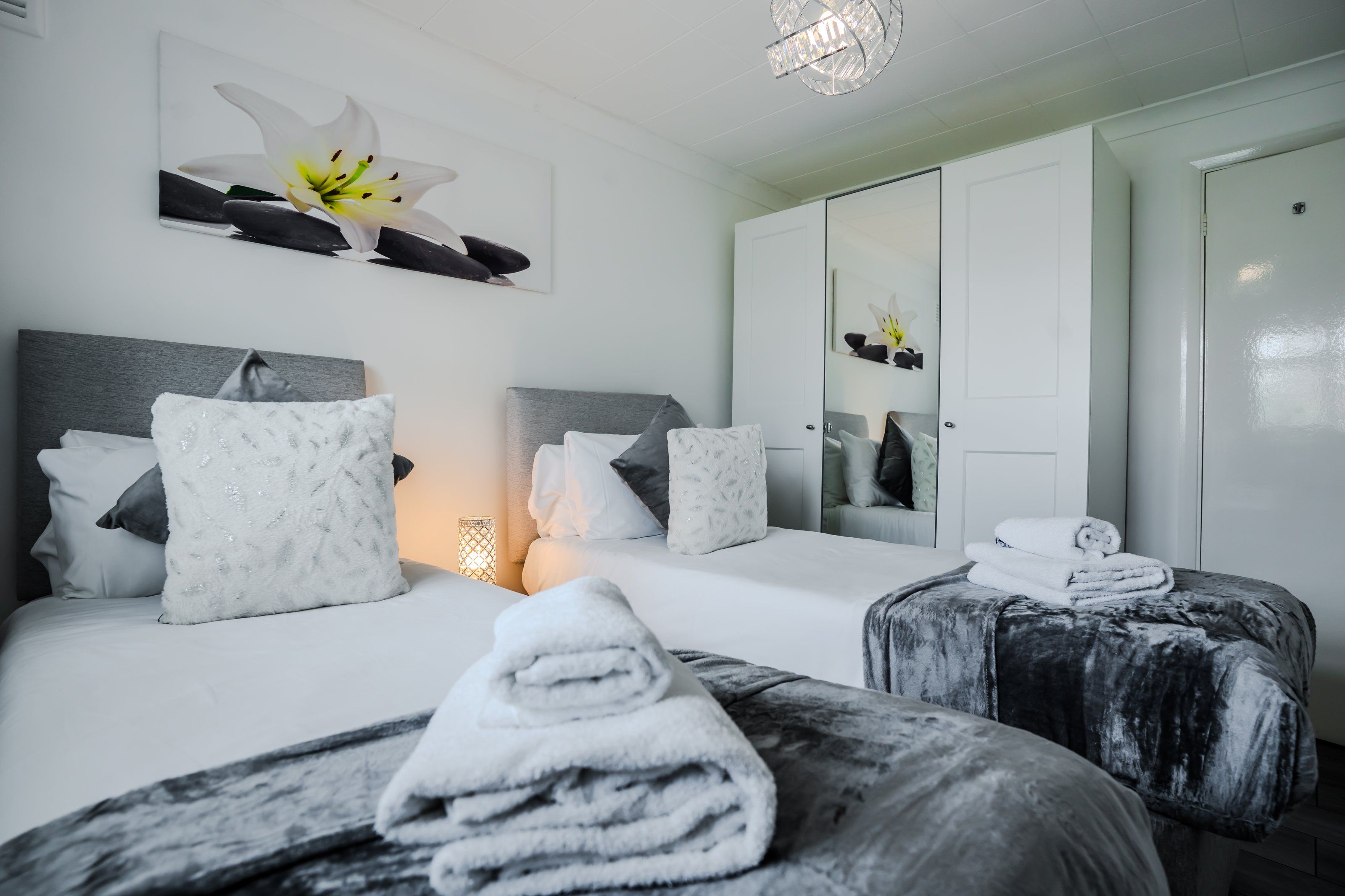A hotel room with two beds, a large mirror, and a chandelier.