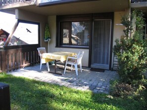 Eine Terrasse im Freien mit Tisch und Stühlen, ein kleiner Garten und ein Blick auf ein Gebäude gegenüber.