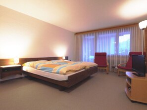 Ein Hotelzimmer mit Bett, Schreibtisch, Stuhl, Fernseher und einem Fenster mit Vorhängen.