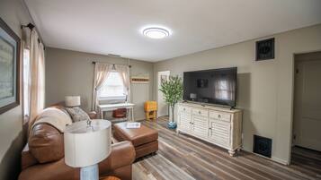 A living room with a brown leather sofa, a television on a white cabinet, and a wooden floor.