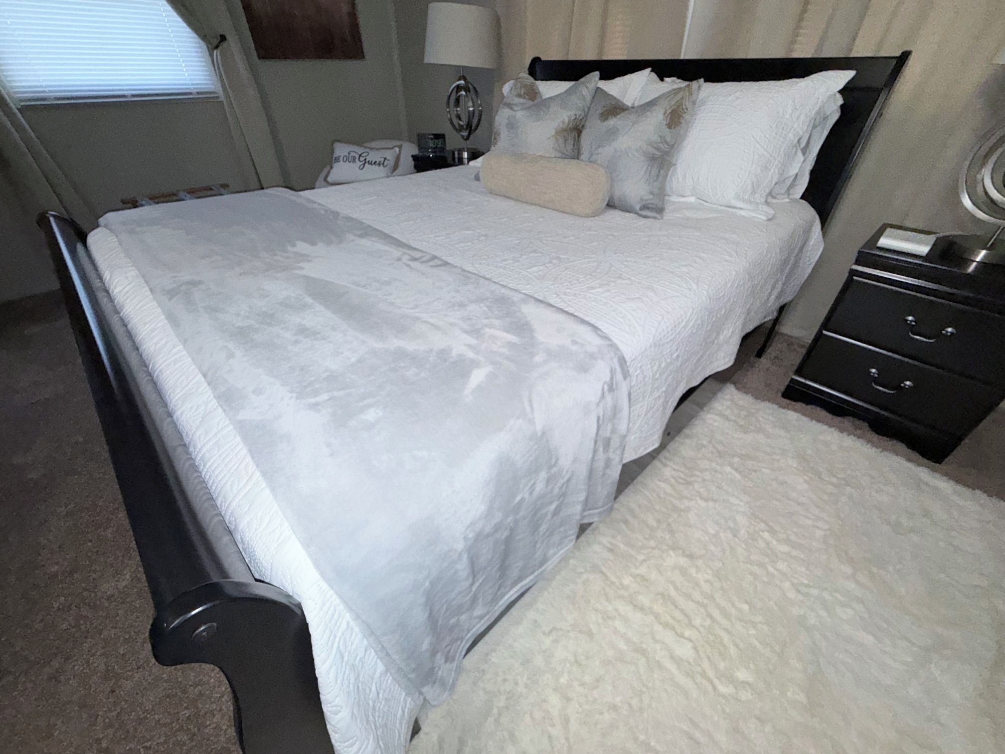 A neatly made bed with a white bedspread, a bedside table with a lamp, and a nightstand with drawers.