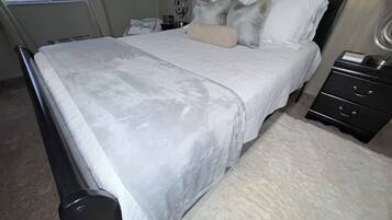 A neatly made bed with a white bedspread, a bedside table with a lamp, and a nightstand with drawers.