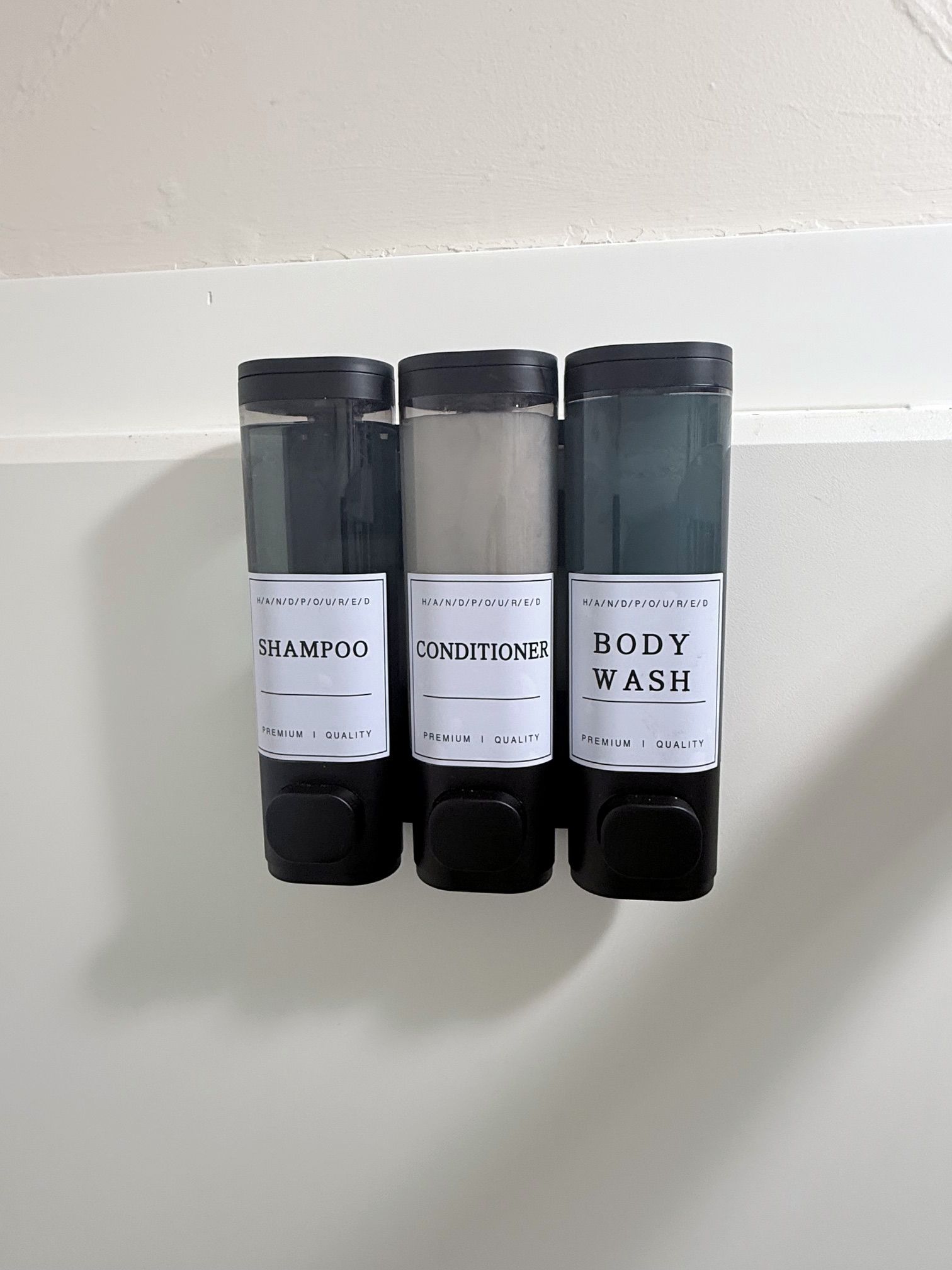Tres botellas de productos para el cabello: champú, acondicionador y jabón de cuerpo, cada una con una etiqueta blanca que indica 'premium quality'.