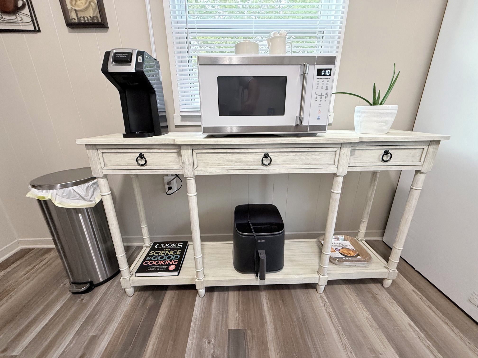 Una kitchenette con microondas, cafetera y un cesto de basura.