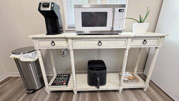 Una kitchenette con microondas, cafetera y un cesto de basura.