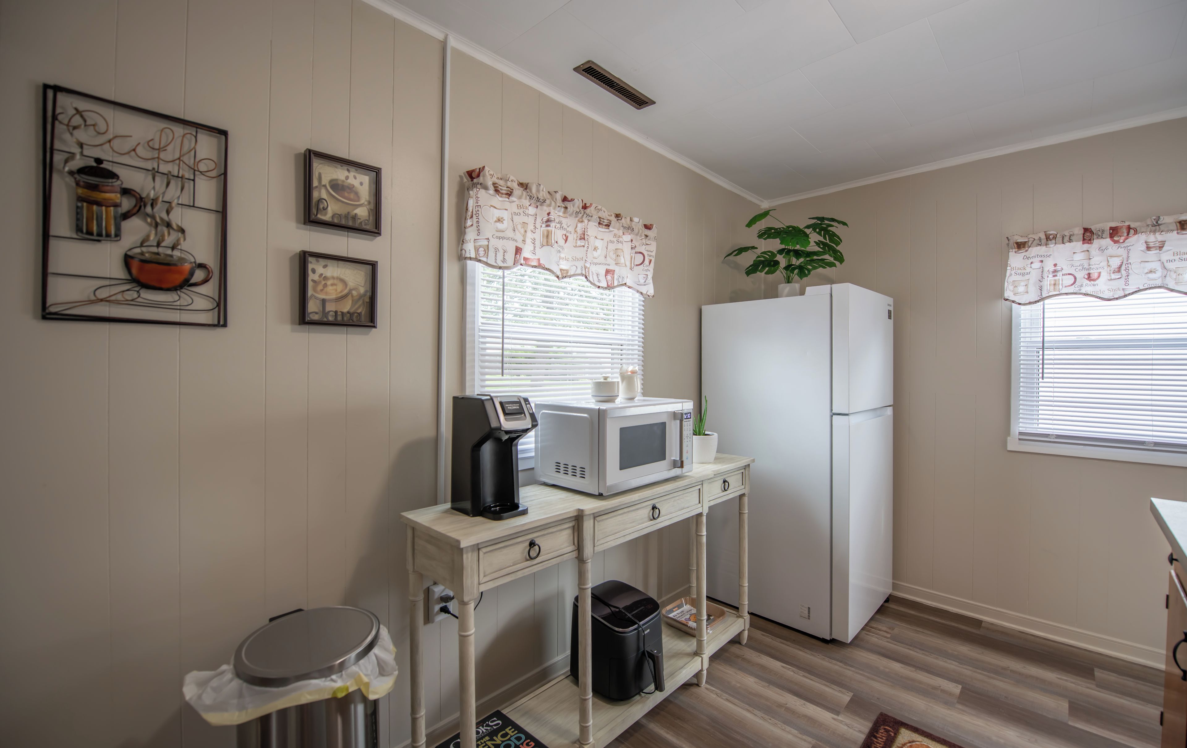 Una cocina con microondas, refrigerador y cafetera sobre una mesa de madera.