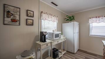 Una cocina con microondas, refrigerador y cafetera sobre una mesa de madera.