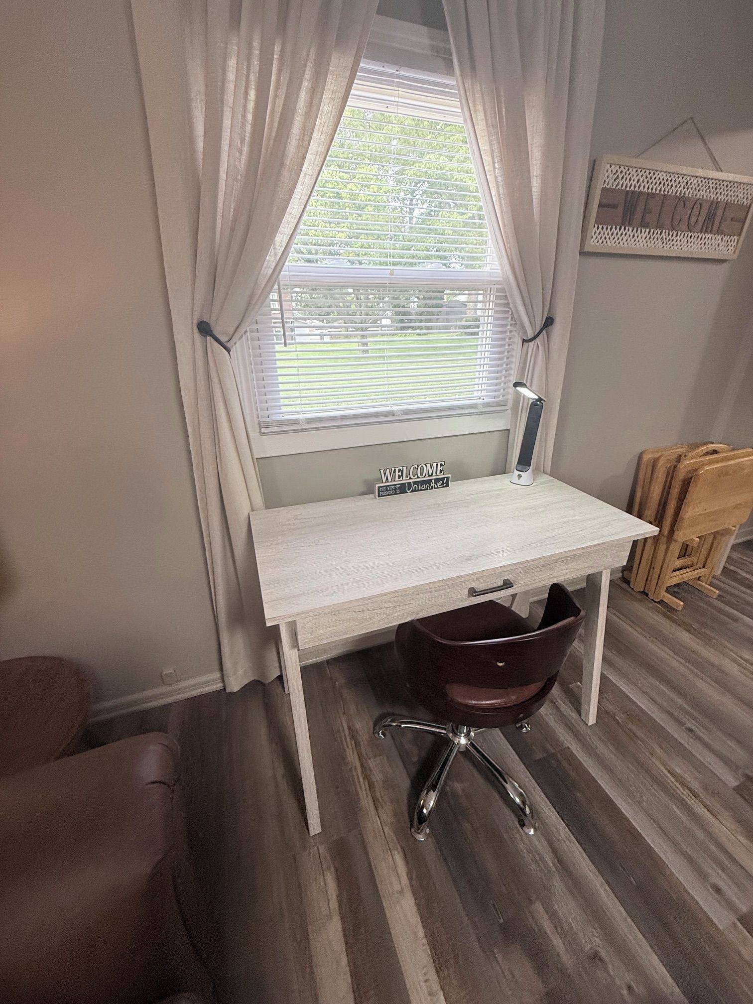 Une pièce comprenant un bureau, une chaise, une fenêtre avec des rideaux et un panneau d’accueil.