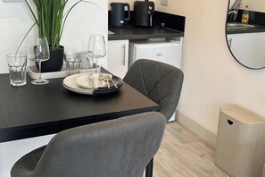 A modern kitchen with a dining table set for two, a potted plant, and a compact refrigerator. - Studio Sleeps 2 with WiFi (Thornton Heath)