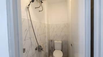 A small bathroom with a toilet, a shower head, and a wall-mounted faucet.
