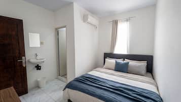 A bedroom with a bed, a bedside table, a mirror, a window with curtains, and a door.