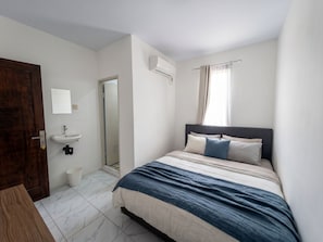 Un dormitorio con una cama, una mesita de noche, un espejo, una ventana con cortinas y una puerta.