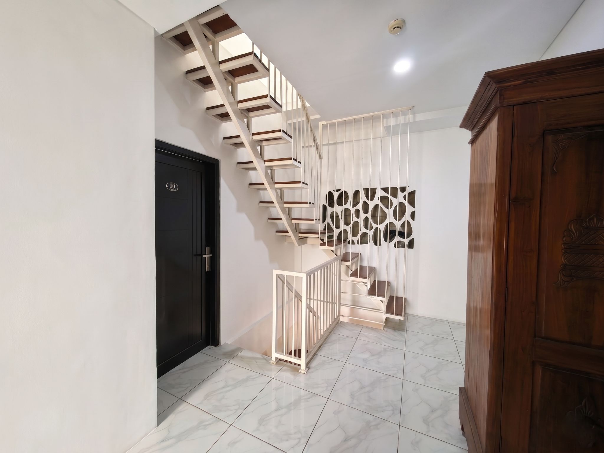 A modern staircase with a white railing, a black door with a number, and a patterned wall.