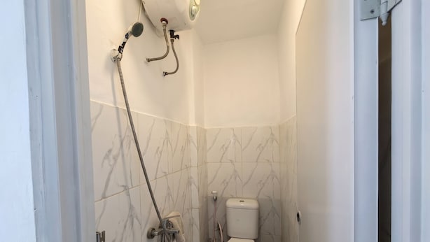 A small bathroom with a toilet, a shower, and a towel rack. - LiviZens at BXC Bintaro Syariah (South Tangerang)