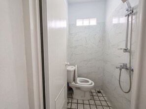 Casa de banho com sanita, chuveiro e paredes com padrão marmorizado.