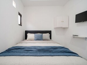 Quarto com cama, guarda-roupa, televisão e uma pequena estante.
