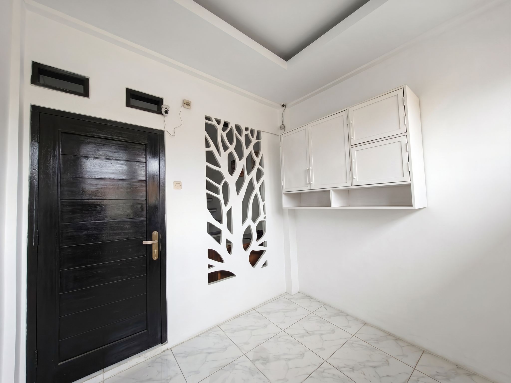 A room with a dark wooden door, a white wall with a decorative panel, and a white cabinet with open shelves.
