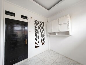 Um quarto com porta de madeira escura, parede branca com detalhe decorativo e armário branco com prateleiras abertas.